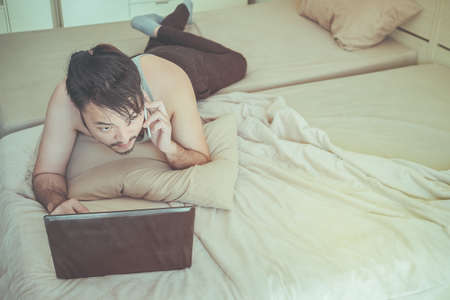 Young man is working in bed after waking up in the morning on a weekend break.の写真素材