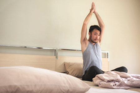 Young man relaxing yoga in bed after waking up in the morning.の写真素材