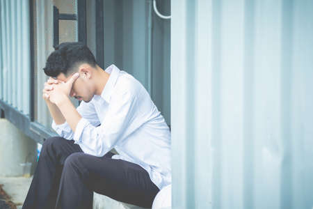 A young man sitting with his hands close to his face and felt sorry for despair in life.の写真素材