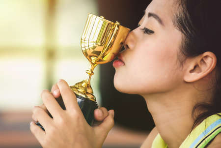 Asian female athlete is kissing her trophy with pride in success.の写真素材