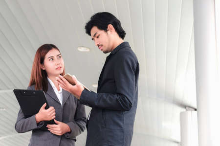 The secretary and the male businessman are discussing and planning the event. They use a tablet and a smartphone to view data.の写真素材