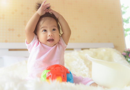 An Asian baby girl is playing in her bed with a happy expression.