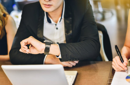 A businessman is looking at his watch to see the appointment.