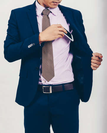An Asian businessman is taking a smartphone from his pocket.の写真素材
