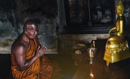 A monk is worshiping and meditating in front of the golden Buddha as part of Buddhist activities.の写真素材