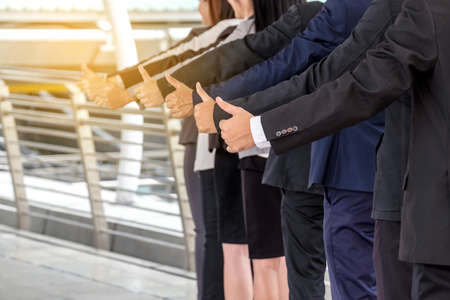 The young Asian business team stands with confidence and pride.They raise their thumbs at the same time.の写真素材