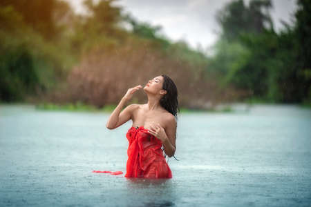 An Asian woman in red bathrobe is enjoying rain and nature in the wild.の写真素材