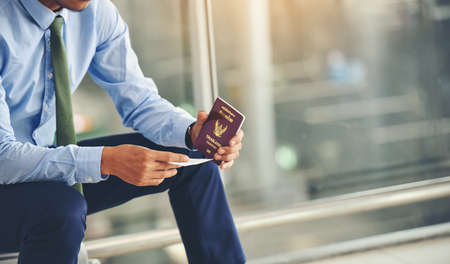 An Asian businessman is holding a plane ticket and his passport is waiting to depart.Focus on hand holding ticket.の写真素材
