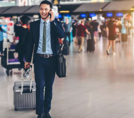 An Asian businessman is using a smartphone to get in business while waiting for a trip in the airport.の写真素材