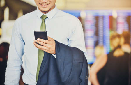 An Asian businessman is using a smartphone to get in business while waiting for a trip in the airport.の写真素材