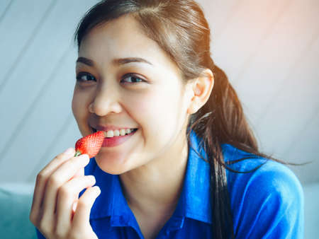 An Asian woman is eating red strawberry for good health, looking young.の写真素材