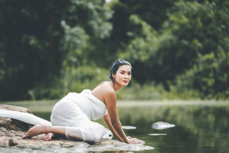 Asian woman in a white bathrobe, enjoying touching water in a stream in the nature.の写真素材