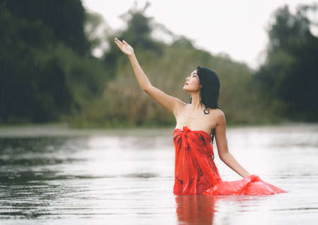 An Asian woman in red bathrobe is enjoying rain and nature in the wild.の写真素材