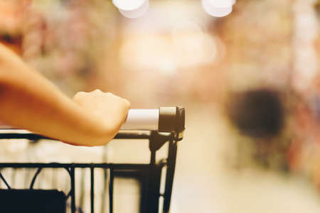Asian woman's hand with supermarket, trolley and many objects that are blurred background.の写真素材