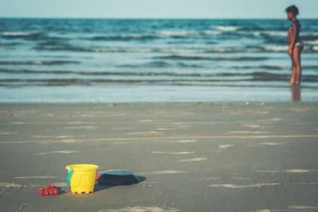 Toys, buckets and shovels that are empty on the sand with the shadow of children and the sea as the background.の写真素材