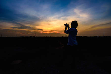 Siluette pictures. Young girls are using a camera. Take a picture of the sunset in front.の写真素材