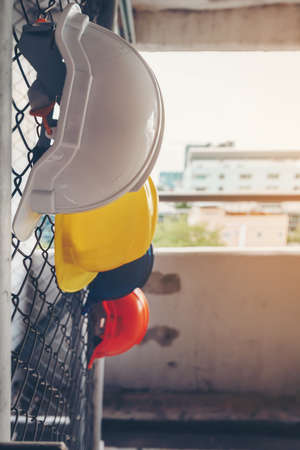 White, yellow, blue and orange helmets that hang on the iron fence at the construction site.の写真素材