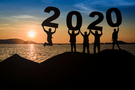 A group of young, sleek silhouettes of people who look happy and ready to hold the numbers 2020 and sunset as the background.の写真素材