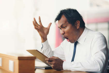 A middle-aged businessman holding a tablet is shocked by what happened to the screen.の写真素材
