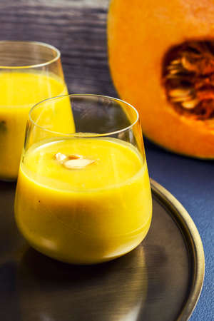 Pumpkin soup with pumpkin seeds in a glass on a golden plateの写真素材