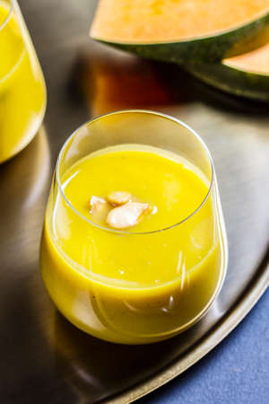 pumpkin soup with pumpkin seeds in a glass on a golden plateの写真素材