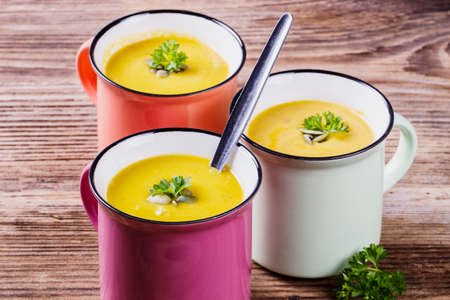 pumpkin soup in colorful enamel mugs with seeds and parsleyの写真素材
