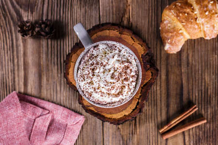 Hot cocoa with whipped cream, a bun and cinnamon on a wooden tableの写真素材