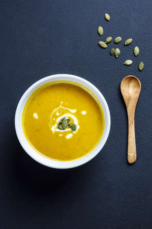 bowl of pumpkin soup, wooden spoon and pumpkin seeds on a dark backgroundの写真素材