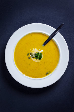 Pumpkin soup with cream, seeds and parsley served in a white plate