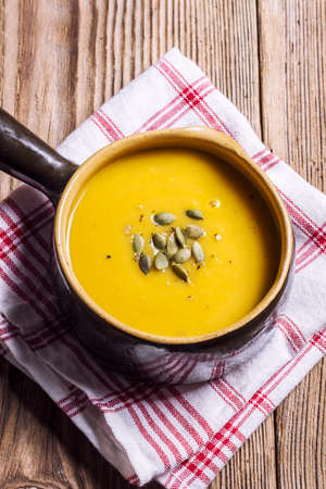 Pumpkin soup in a brown, ceramic bowl on a wooden tableの写真素材