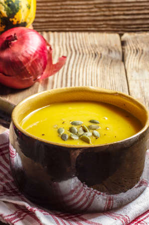 Pumpkin soup in a brown, ceramic bowl on a wooden tableの写真素材