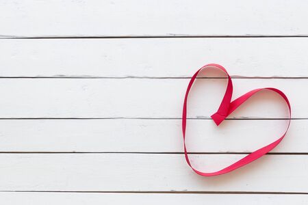 Red fabric ribbon form to be heart symbol on white wooden background for valentine and love conceptの写真素材