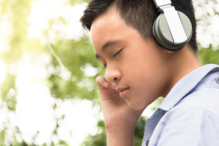Portrait boy wearing headphones listening some music at outdoor and his feeling look like be in a dreamy stateの写真素材