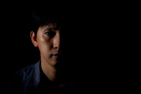 Close up portrait of a man on black background with half face in shadow and copyspaceの写真素材