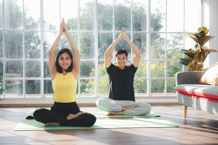 Couple of Asian boy and Asian young girl practicing yoga on mats in living room at home