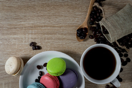 Black Coffee in a cup with coffee beans and macarons on wood table background