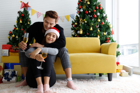 Beautiful young Asian couple is holding glasses of champagne, smiling and affectionate while celebrating New Year at homeの写真素材
