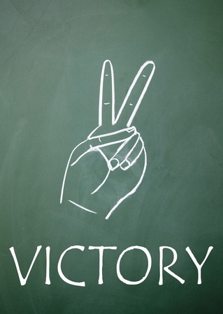 Victory sign drawn with chalk on blackboardの写真素材