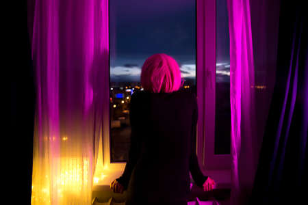 A lonely girl with pink hair looks out the window.の写真素材