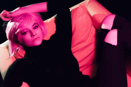 Fashion sexy woman pink hair on the armchair . Pink light. Life style. Retro wave neon noir lights color toningtの写真素材