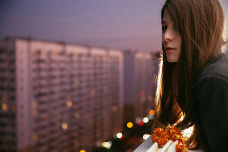 Young natural beauty long hair girl with flowers on the balcony. Spring. Evening. High-rise area. Portraitの写真素材