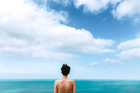 slim girl with a beautiful bare back is standing on the sea. Blue sky with clouds. Unity with nature. freedomの写真素材