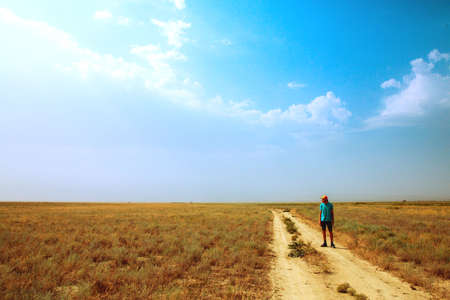 young man standing in the savannah. Heat, sun, blue sky. dry groundの写真素材