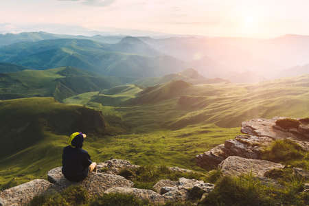 Travel man tourist sitting alone on the edge mountains over green valley adventure lifestyle extreme vacations green landscapeの写真素材