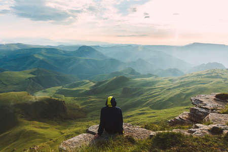 Travel man tourist sitting alone on the edge mountains over green valley adventure lifestyle extreme vacations green landscapeの写真素材