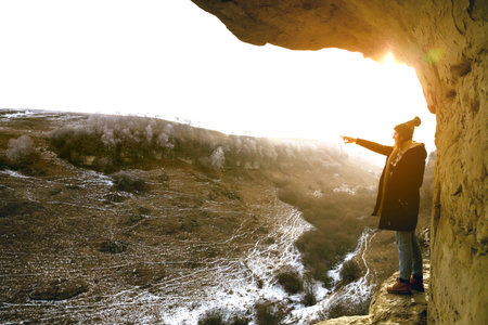A smiling beautiful woman in a hat is standing in the mountains. The sun. Winter