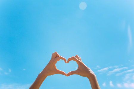 Heart shape making of hands against blue sky