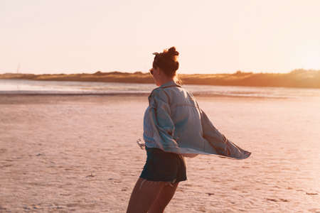 Young stylish hipster girl dancing Jeans jacket Sunset coast during travel summer holidays vacation outdoorsの写真素材