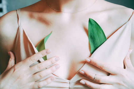 Tender beautiful female body in a light dress and green leaves. gentle Spring themeの写真素材