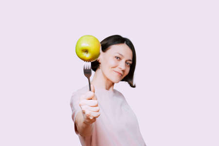 Young Woman holds in hand a fork with green apple on a light background. Healthy organic food for dieting woman conceptの写真素材